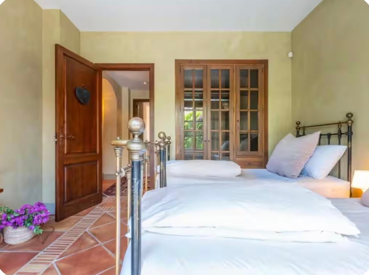 Twin bedroom with brass beds, white linen and garden views